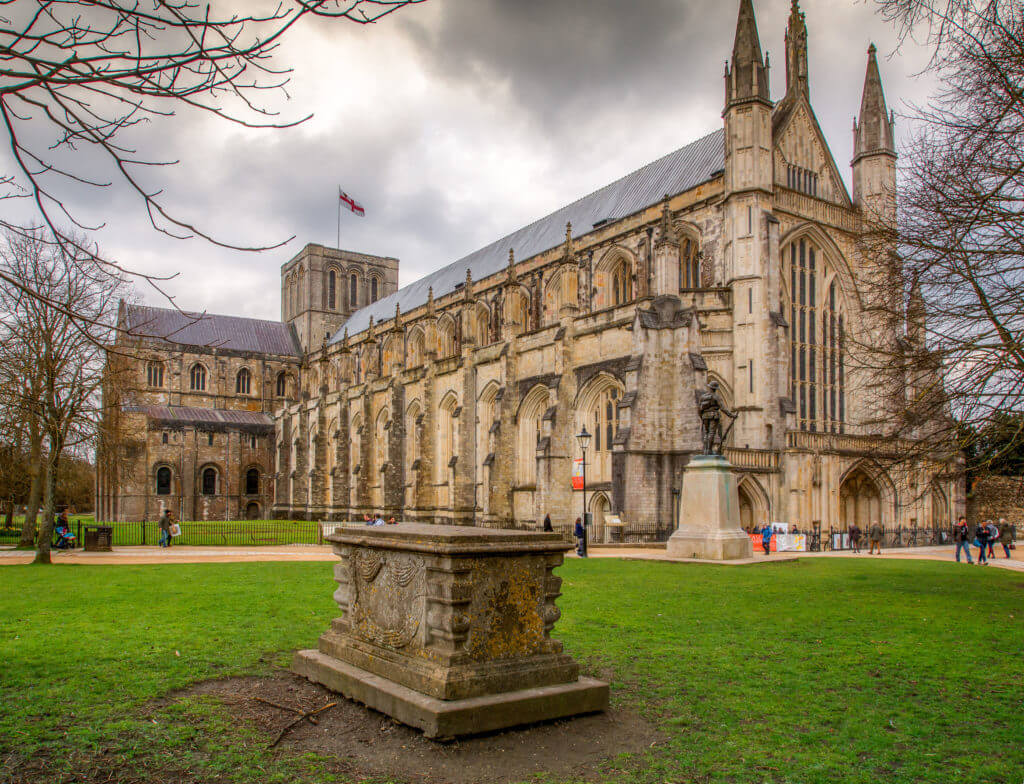 Winchester Cathedral with dramatic clouds and tomb in the foreground