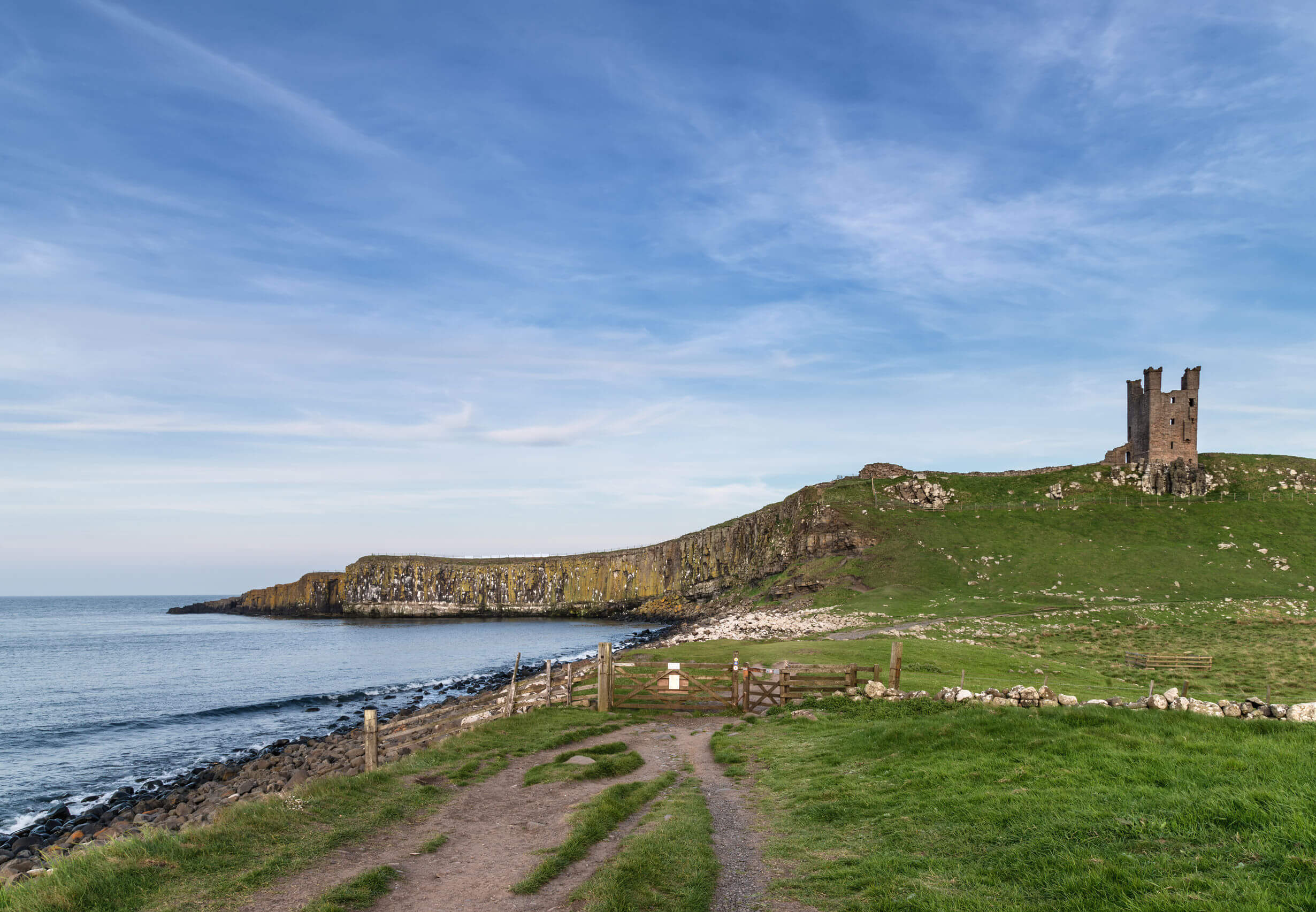 Beautiful landscape image of Dunstanburgh Castle on Northumberland coastline in England during late Spring evening