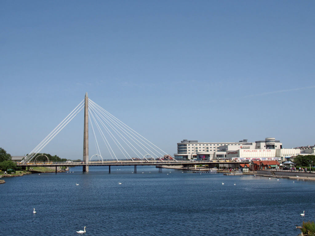 southport, merseyside, united kingdom - 28 june 2019: the suspension bridge and pier crossing the lake in southport merseyside with a view of the town hotels and buildings