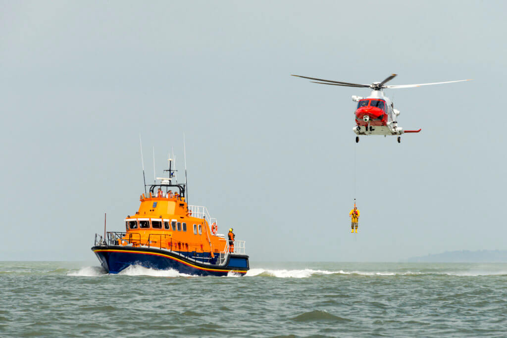 orange sea rescue boat at sea off south coast of Britain man being winched to emergency rescue helicopter