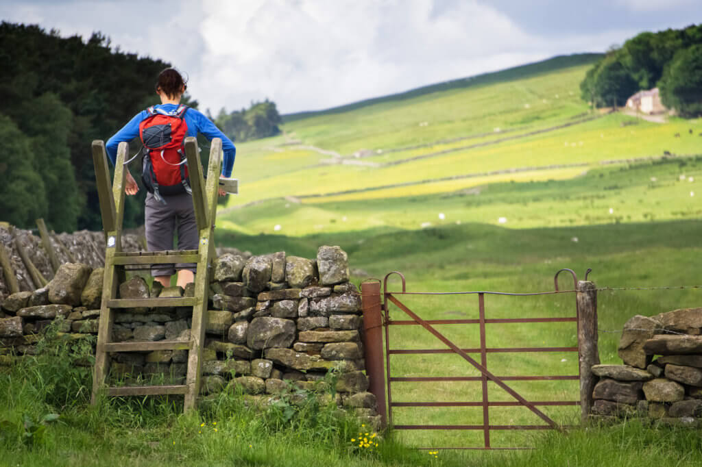 A hiker crossing a stile on the Hadrians Wall Walk in Northumberland, North East of England, UK.