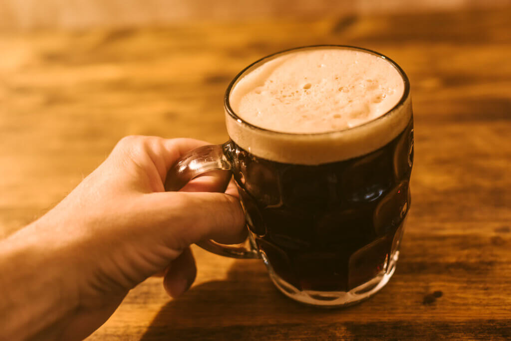 Man drinking dark beer in british dimpled glass pint mug on bar table