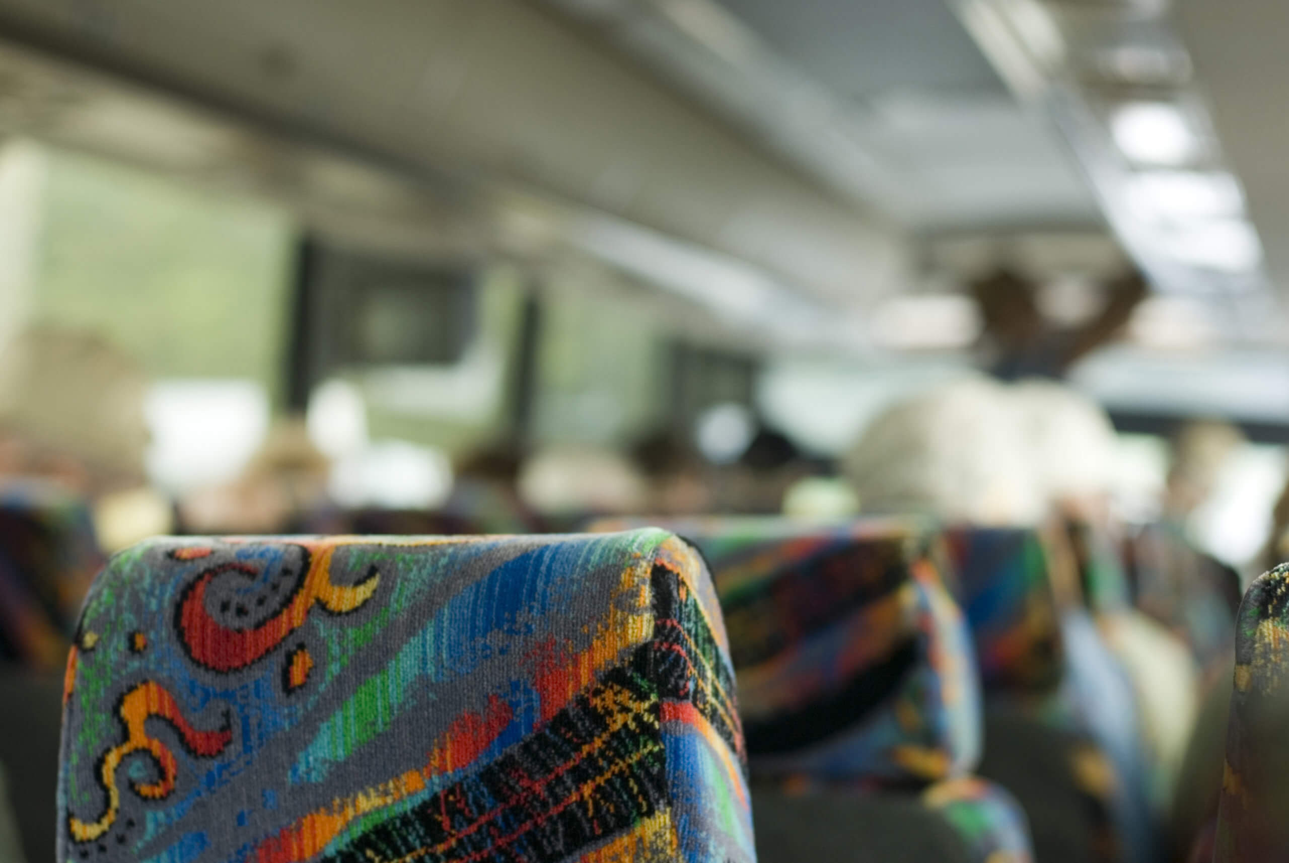 Blurred background showing the interior of a tour coach bus with focus to the floral fabric back of a passenger seat in the foreground